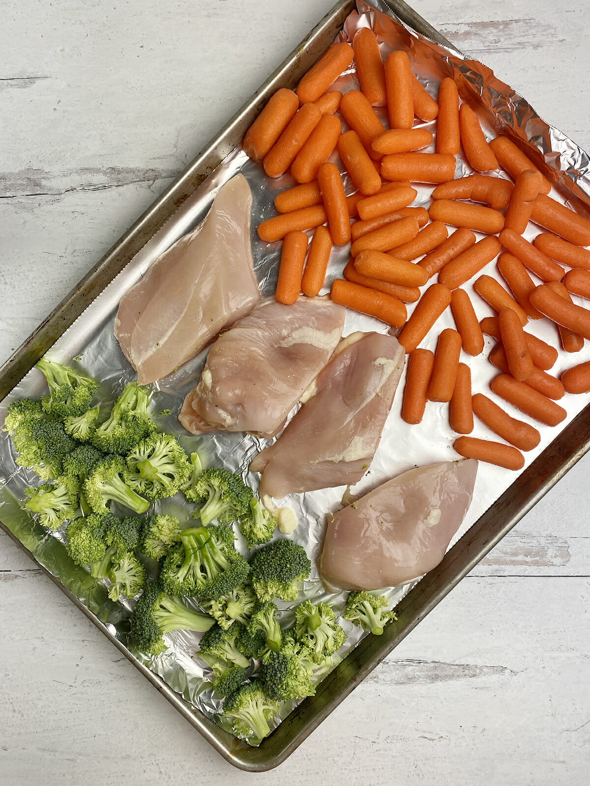 One pan roasted chicken and veggies on a pan ready for the oven.