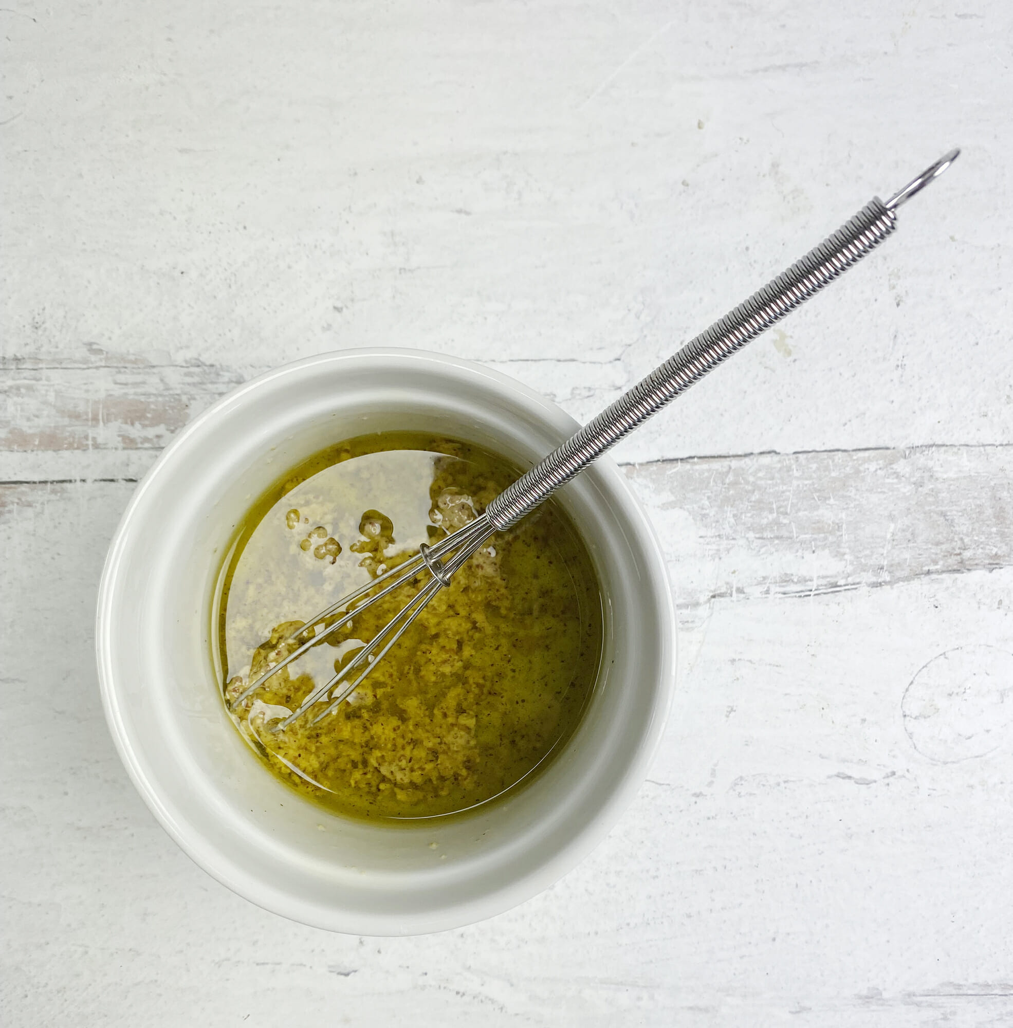 Olive oil and mustard in a little bowl with a whisk.