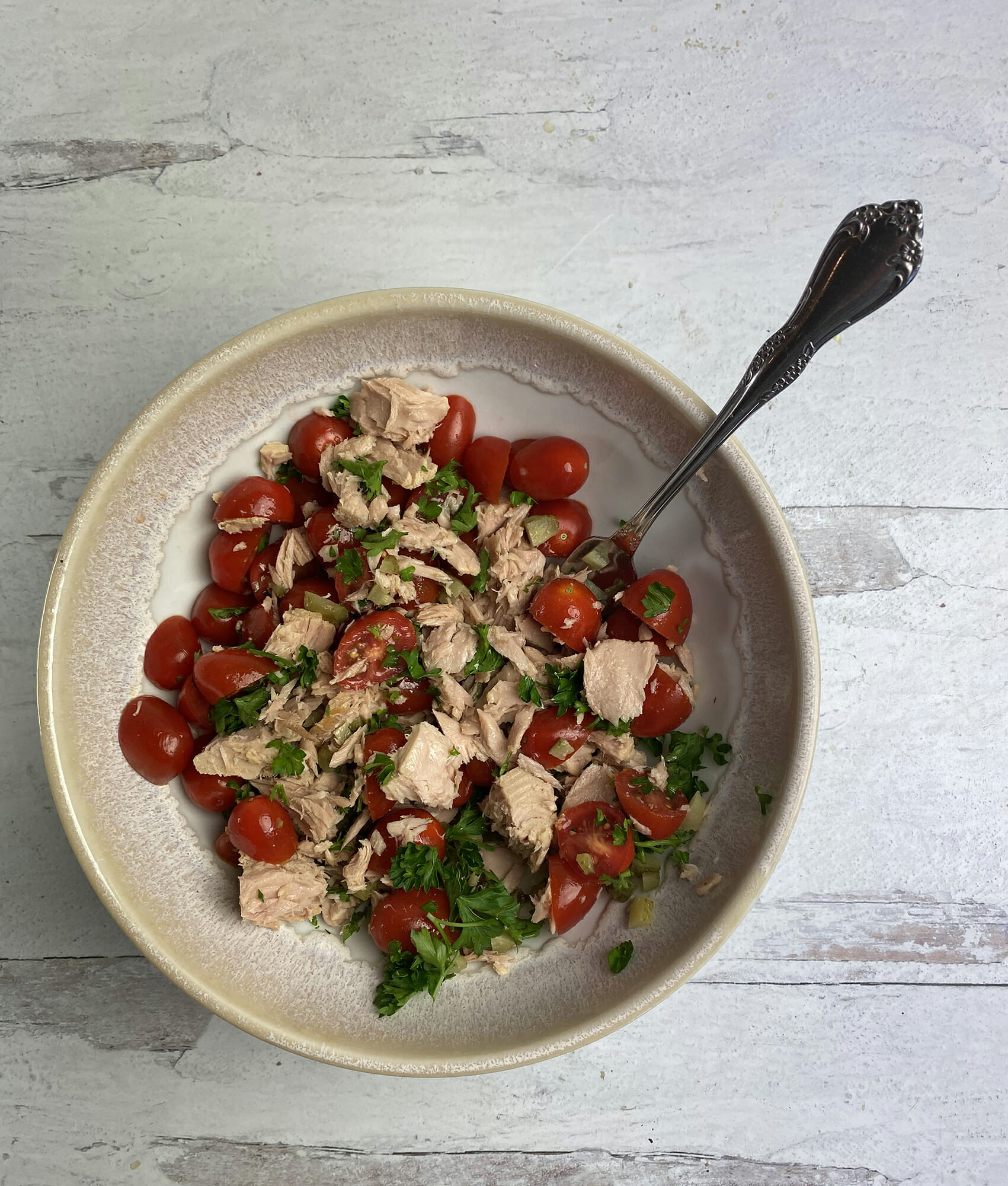Tuna fish in a bowl with cherry tomatoes and parsley.
