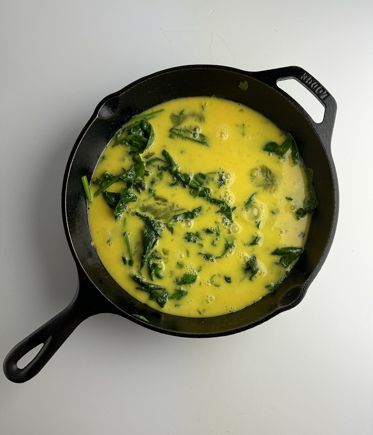 Beaten eggs and spinach in a skillet.