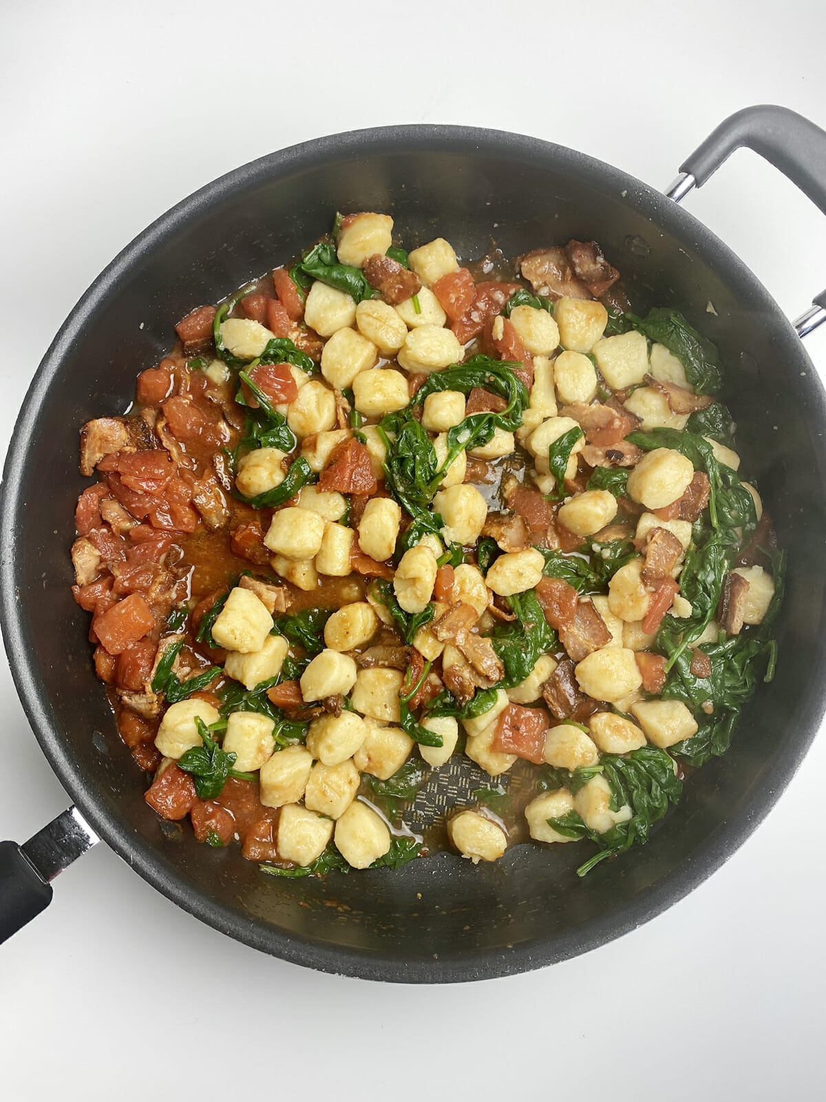 Gnocchi with bacon spinach sauce in a skillet.