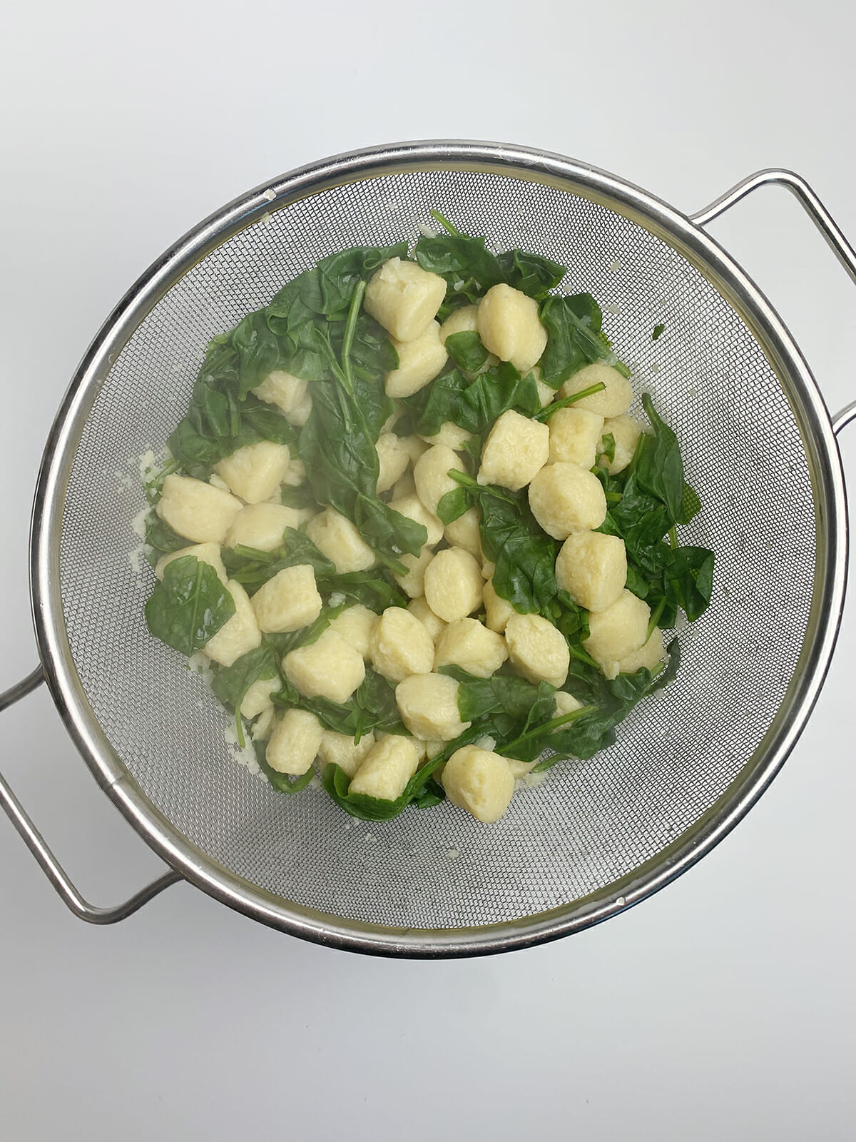 Gnocchi and spinach draining in strainer.