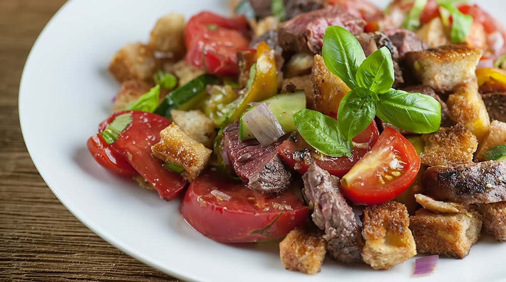 Steak panzanella salad on a white plate.