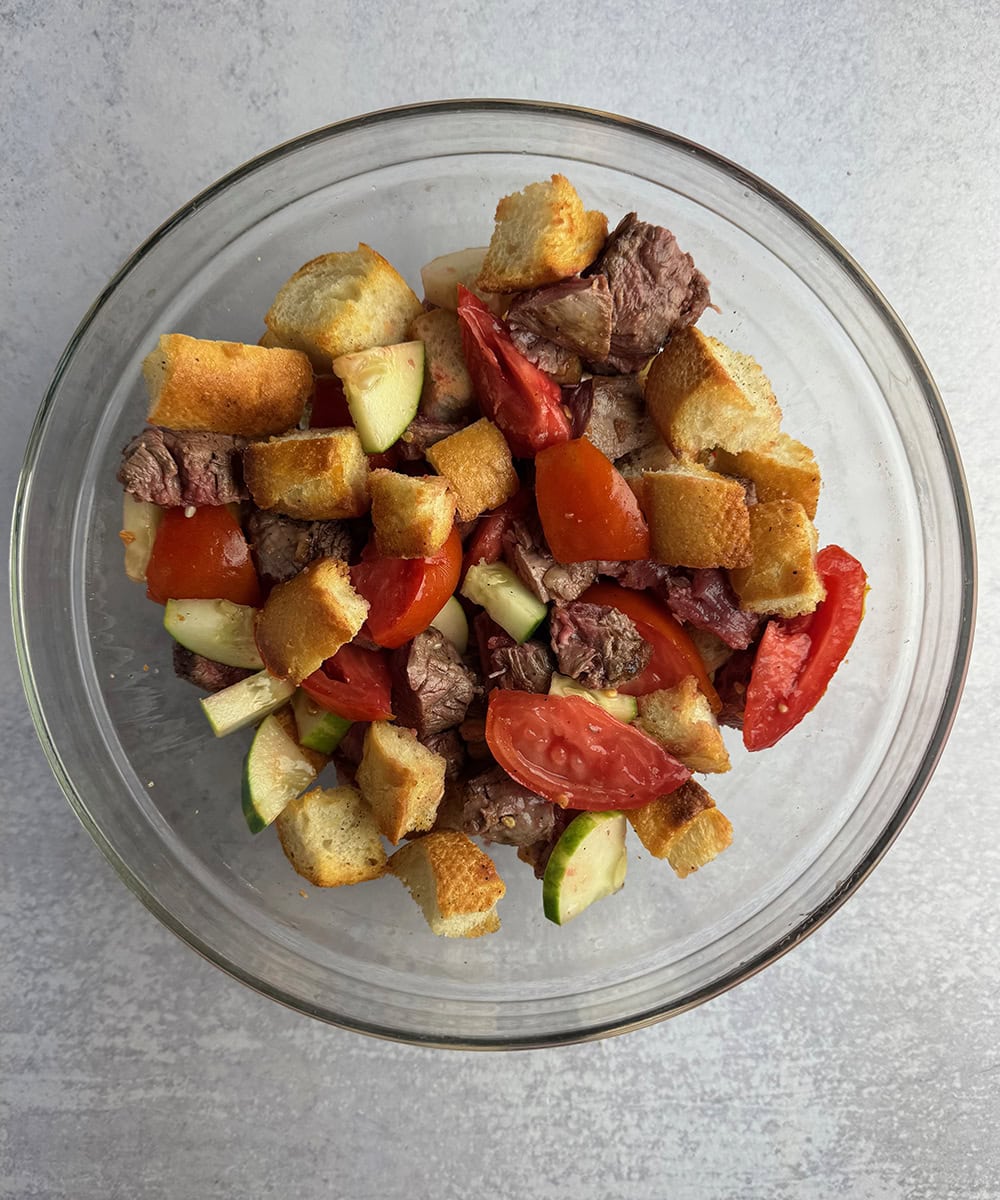 Steak tomatoes and bread cubes in a bowl.