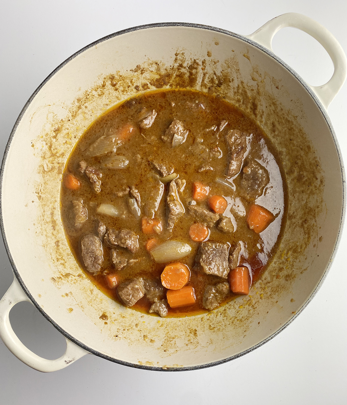 Mustard beef stew in a pot with vegetables added.