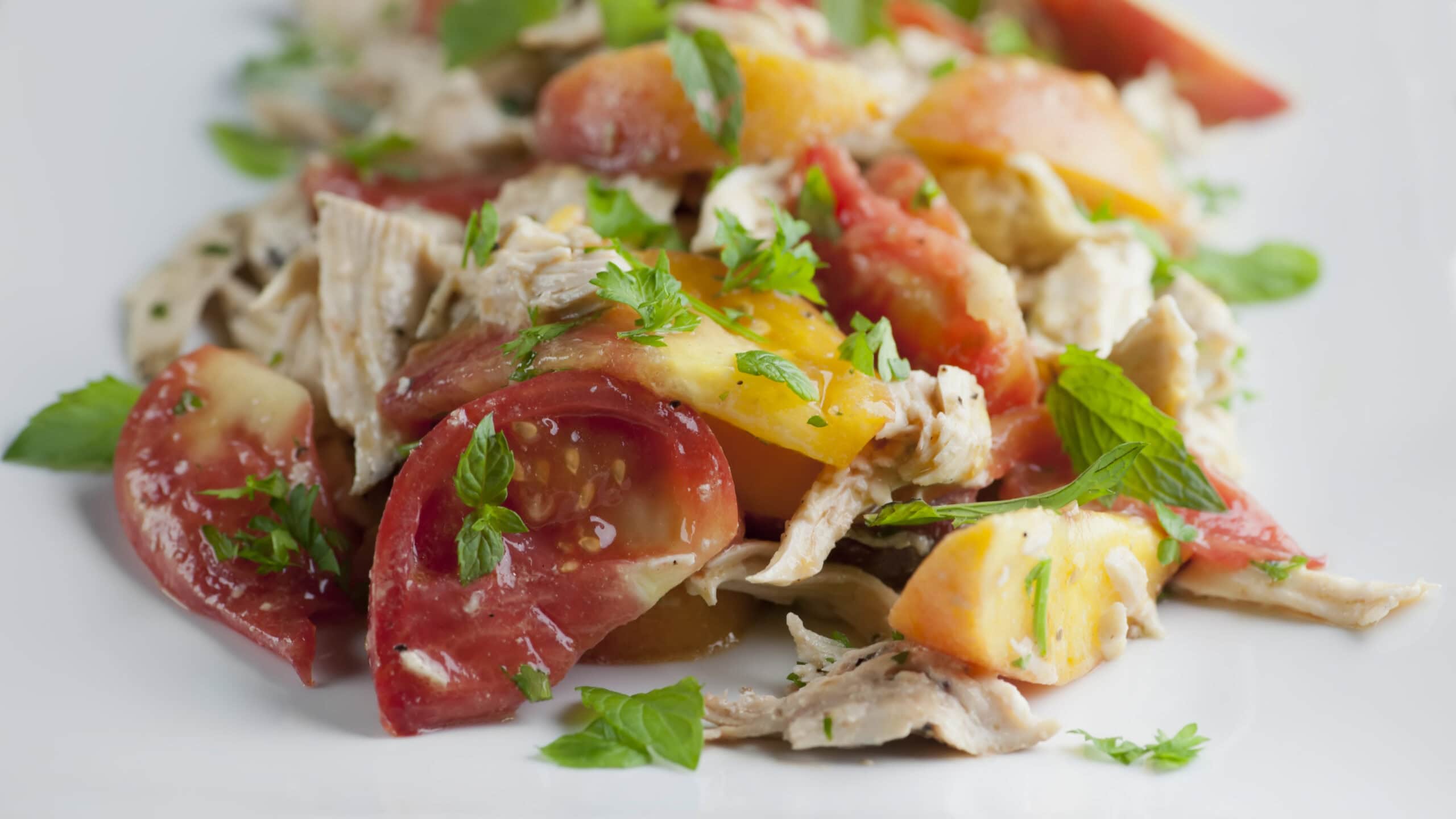 Tomato peach chicken salad ingredients on a plate.