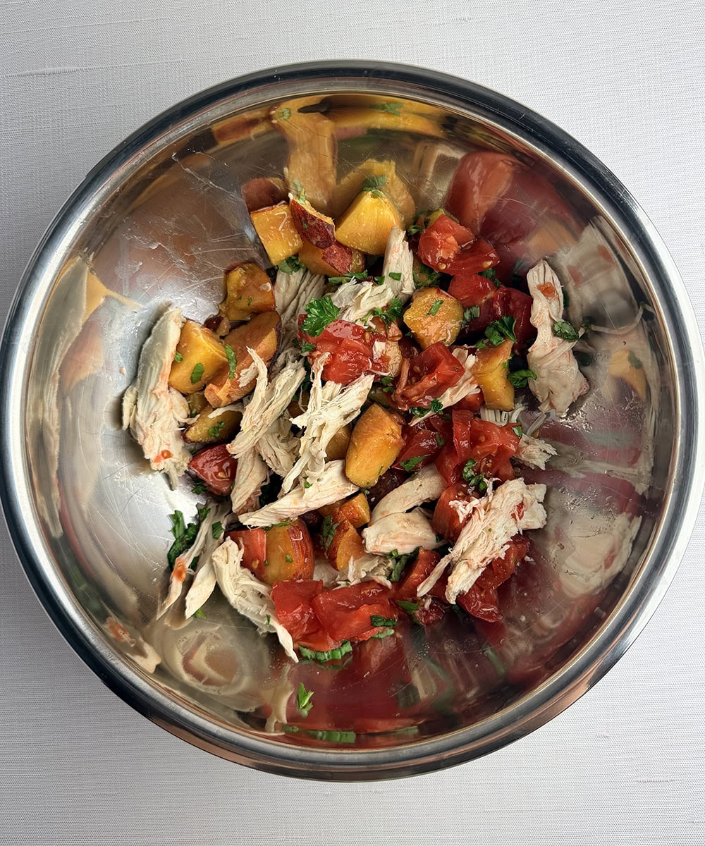 Tomato peach chicken salad ingredients in a bowl.