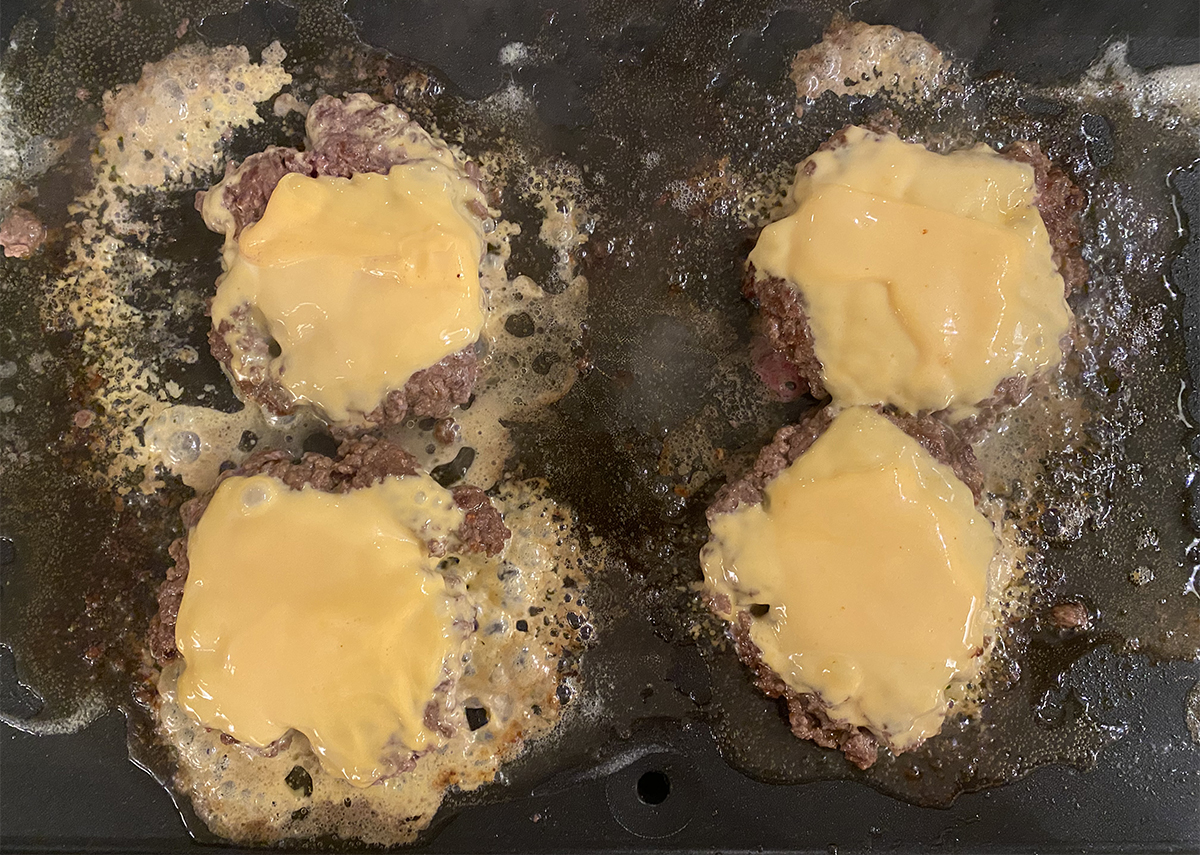 Cheese melting on diner burgers on a griddle.