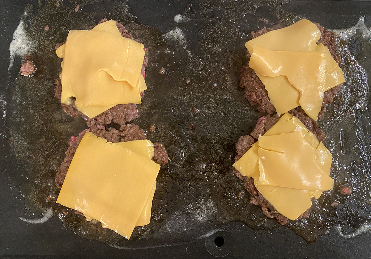 Diner burgers with cheese added on a griddle.