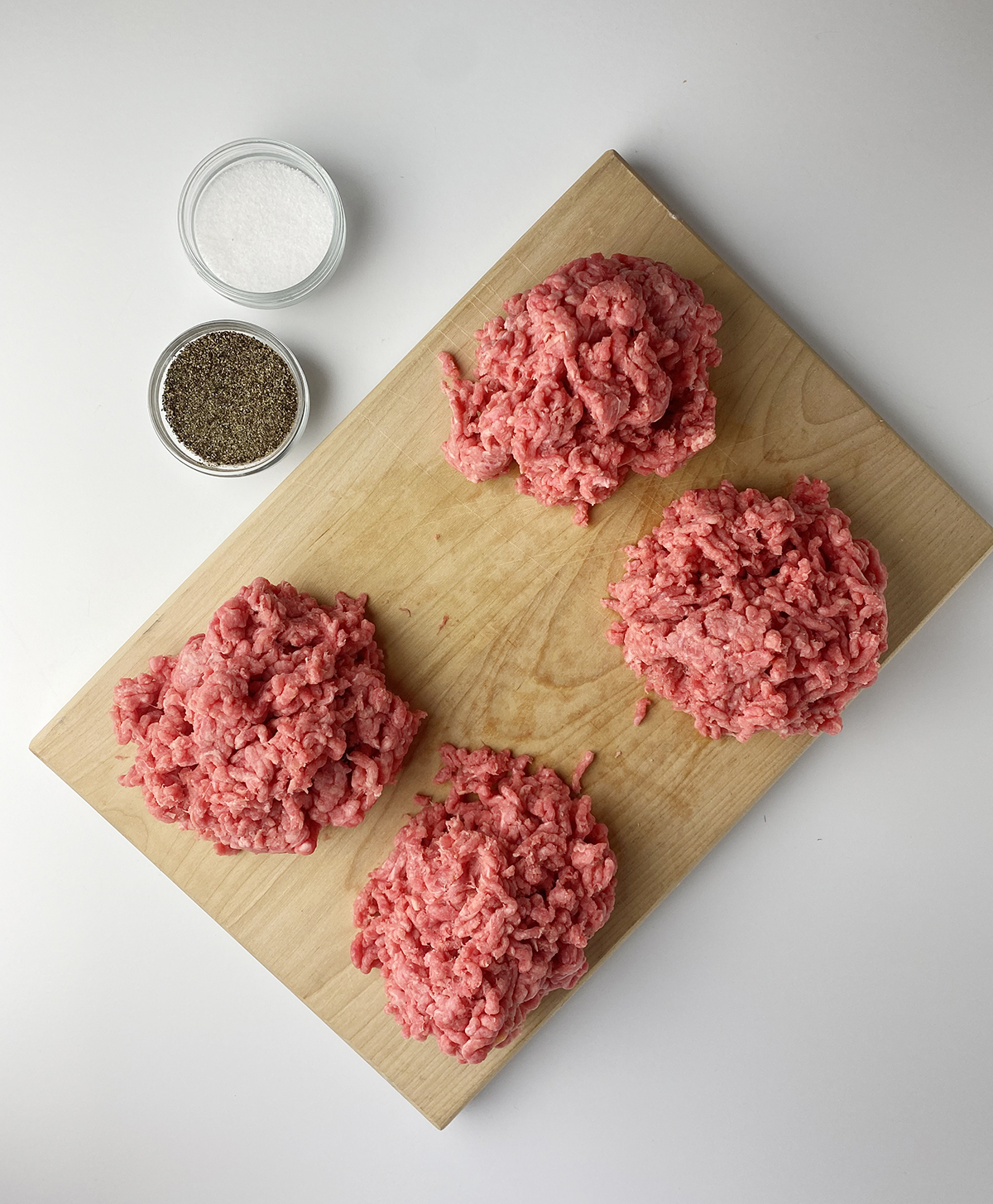 Piles of ground beef for burgers on a wooden board.