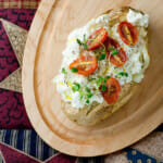 Baked potato with ricotta and tomatoes on a wooden board.