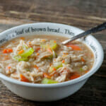 Bowl of slow cooker chicken barley soup on a wooden counter.
