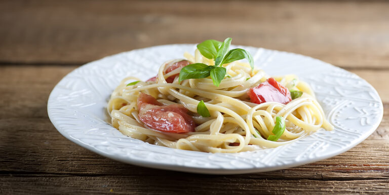Pasta with brie tomatoes and basil on a plate.