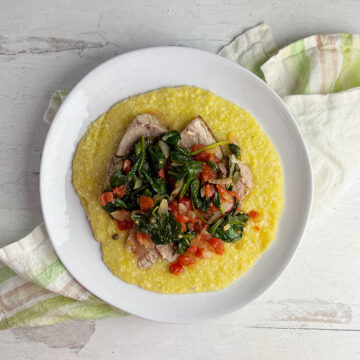 Seared tuna with tomato spinach sauce on a plate with grits.