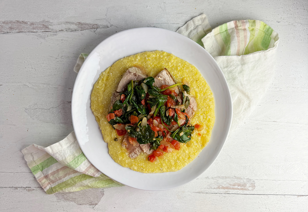 Seared tuna with tomato spinach sauce on a plate with grits.