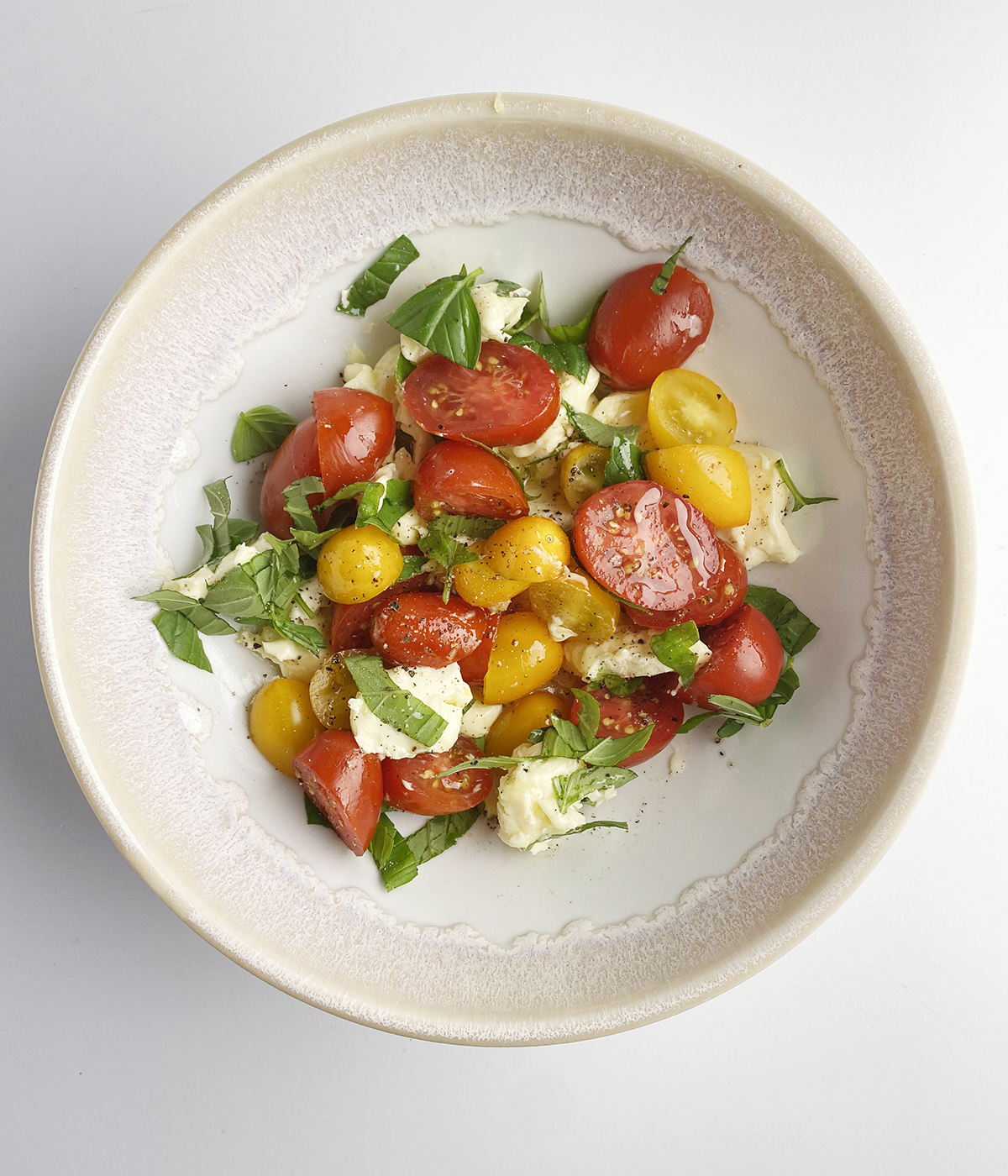 Tomatoes Brie cheese and basil marinating in a bowl.