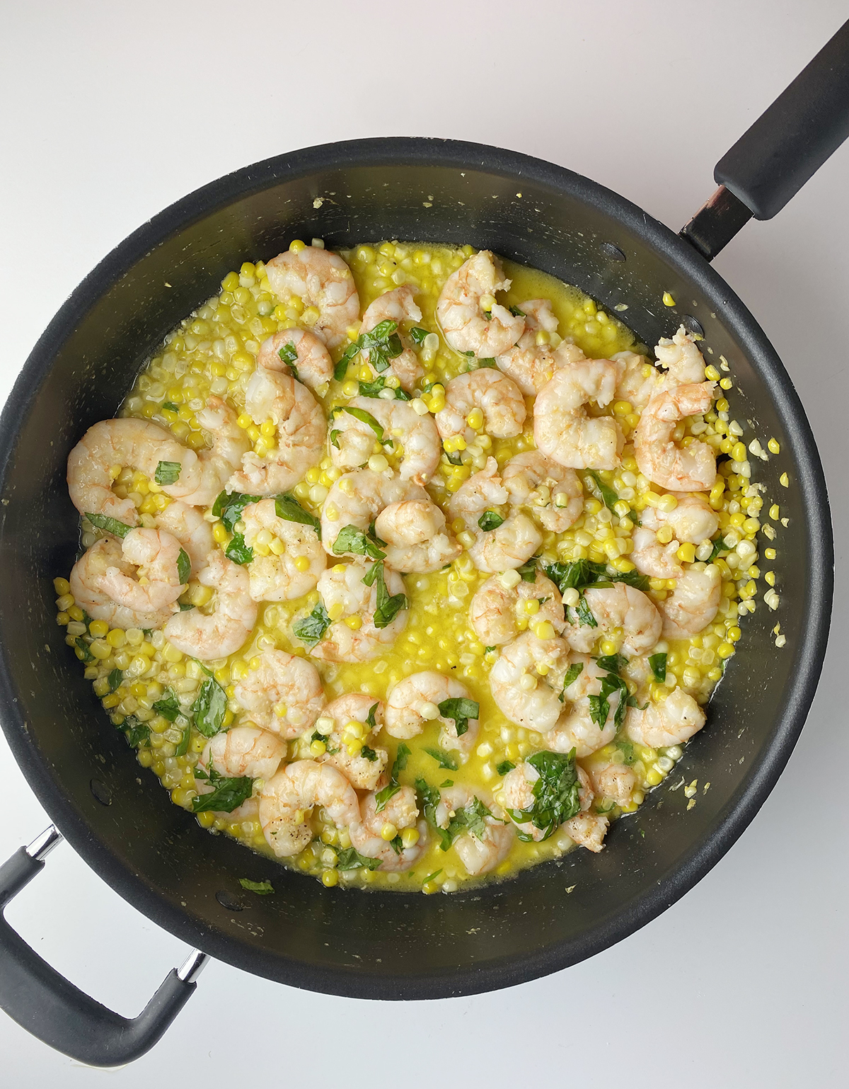 Buttered shrimp and corn in skillet with herbs sprinkled in.