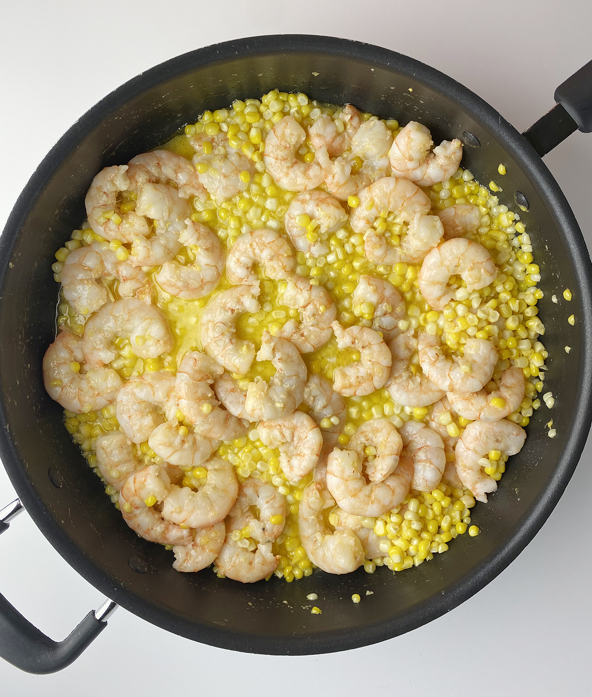 Shrimp and corn cooking in a skillet.