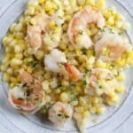 Buttered shrimp with corn and herbs on a plate.