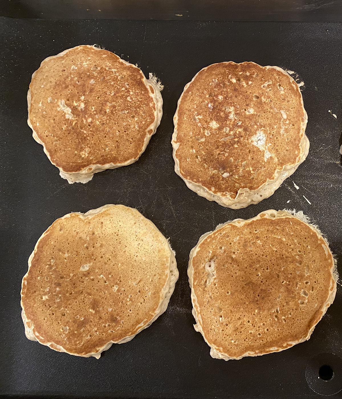 Cinnamon oat pancakes cooking on a griddle.