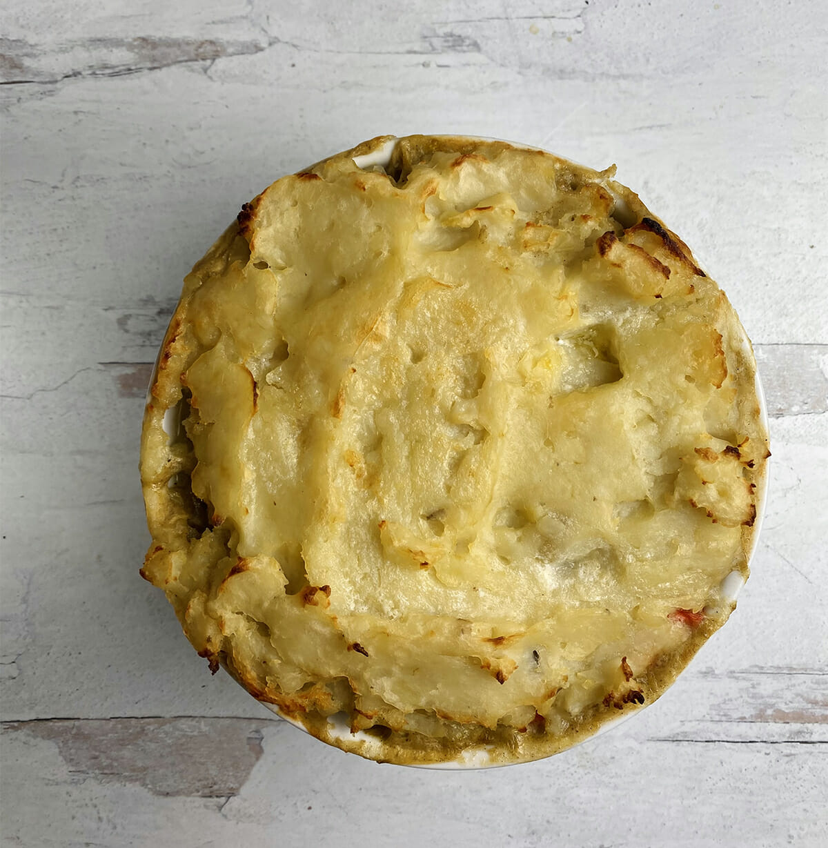Baked chicken pot pie with a mashed potato crust on a wooden counter.