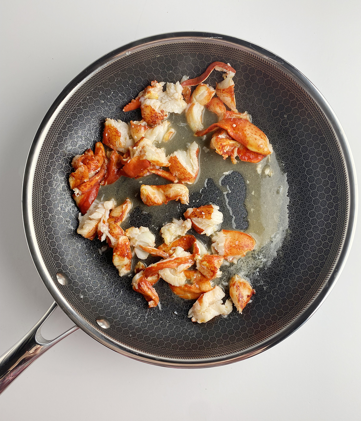 Lobster pieces warming in butter in a skillet.