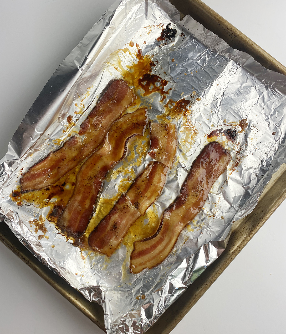 Cooked bacon strips on a foil-lined pan.