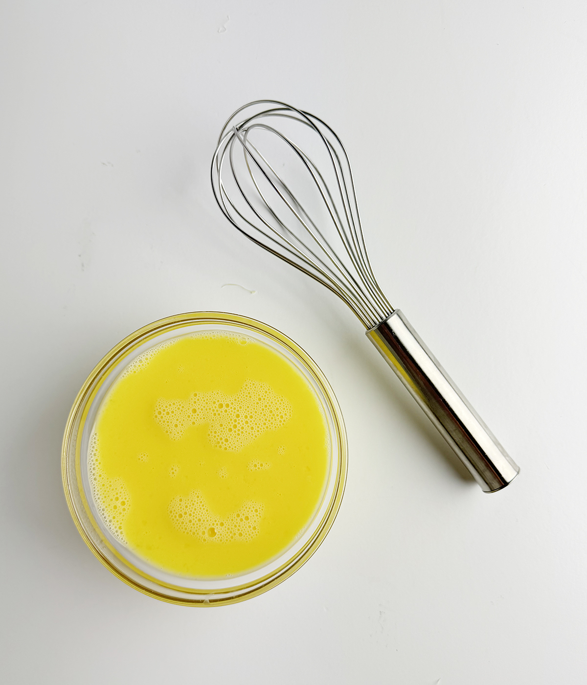 Bowl of beaten egg with a whisk.