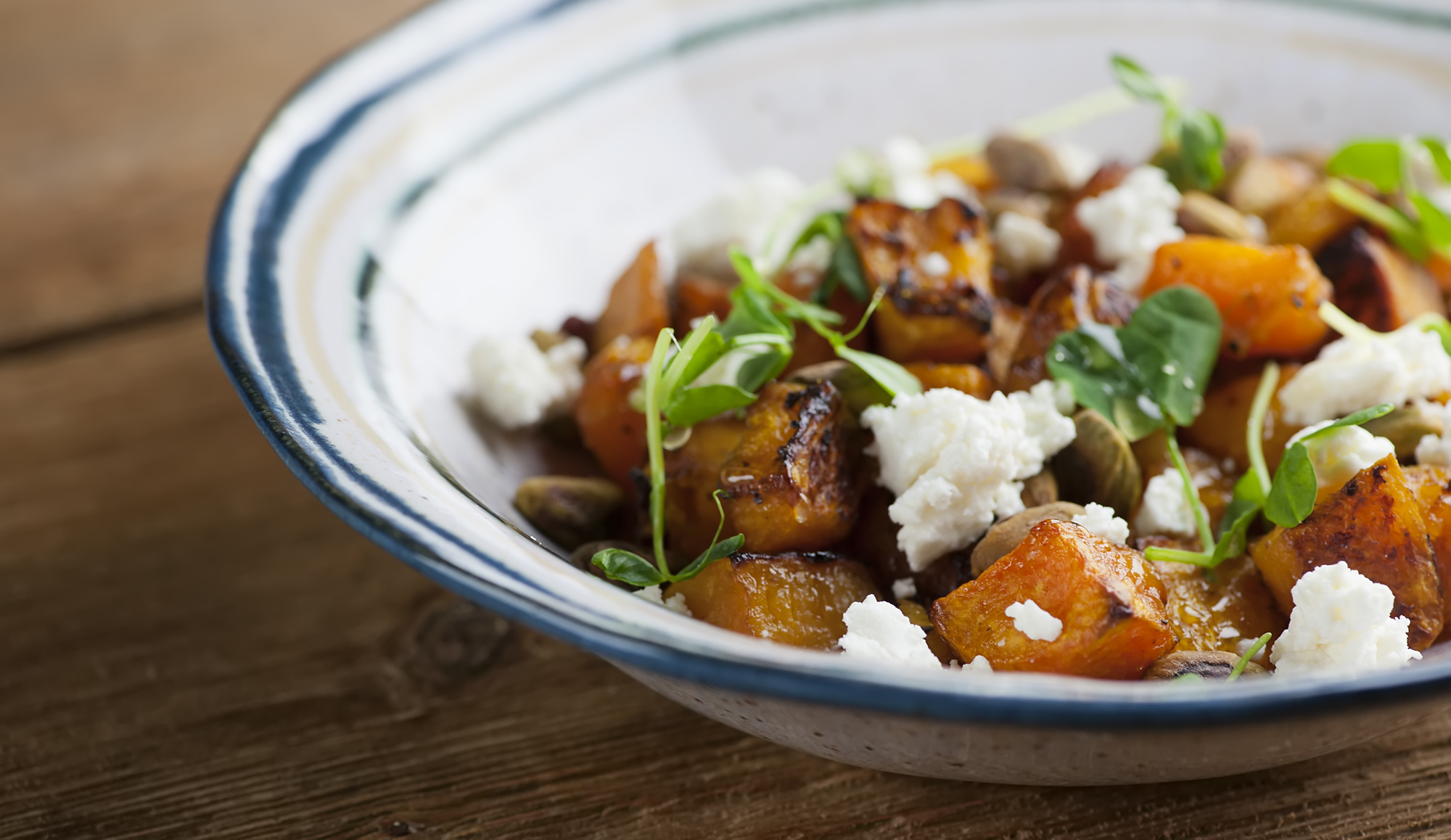 A bowl of roasted butternut squash with feta cheese and microgreens.