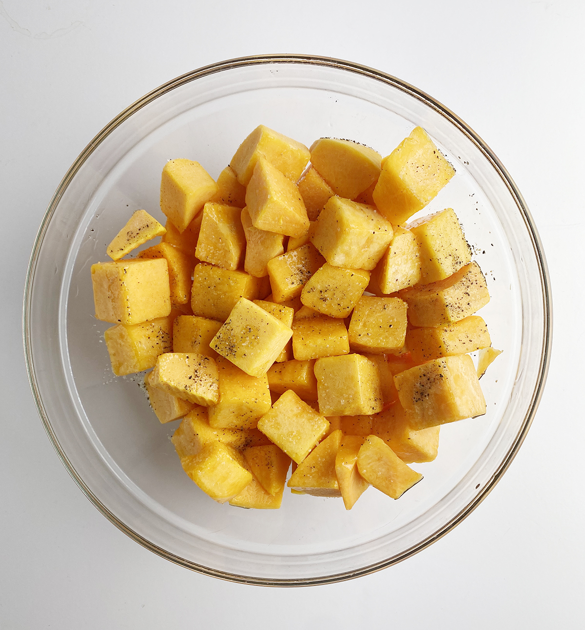 butternut squash cubes in bowl tossed with olive oil and pepper.