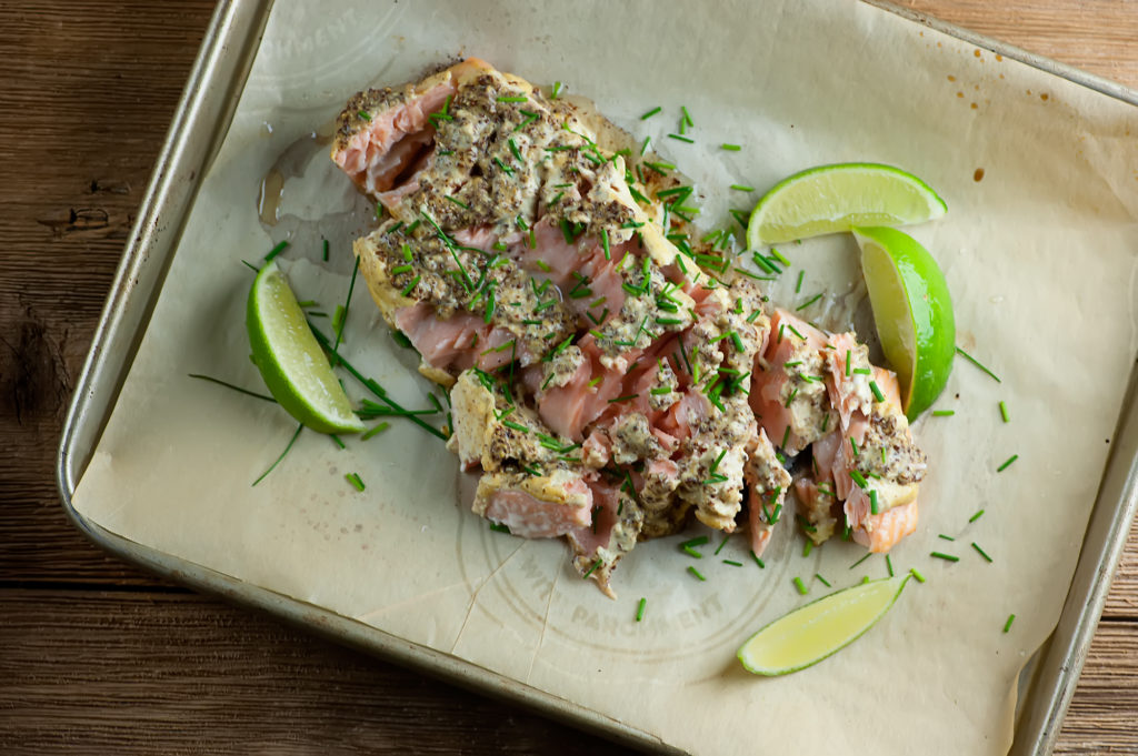 mustard lime roasted salmon Salmon with mustard sauce and limes on a baking sheet.