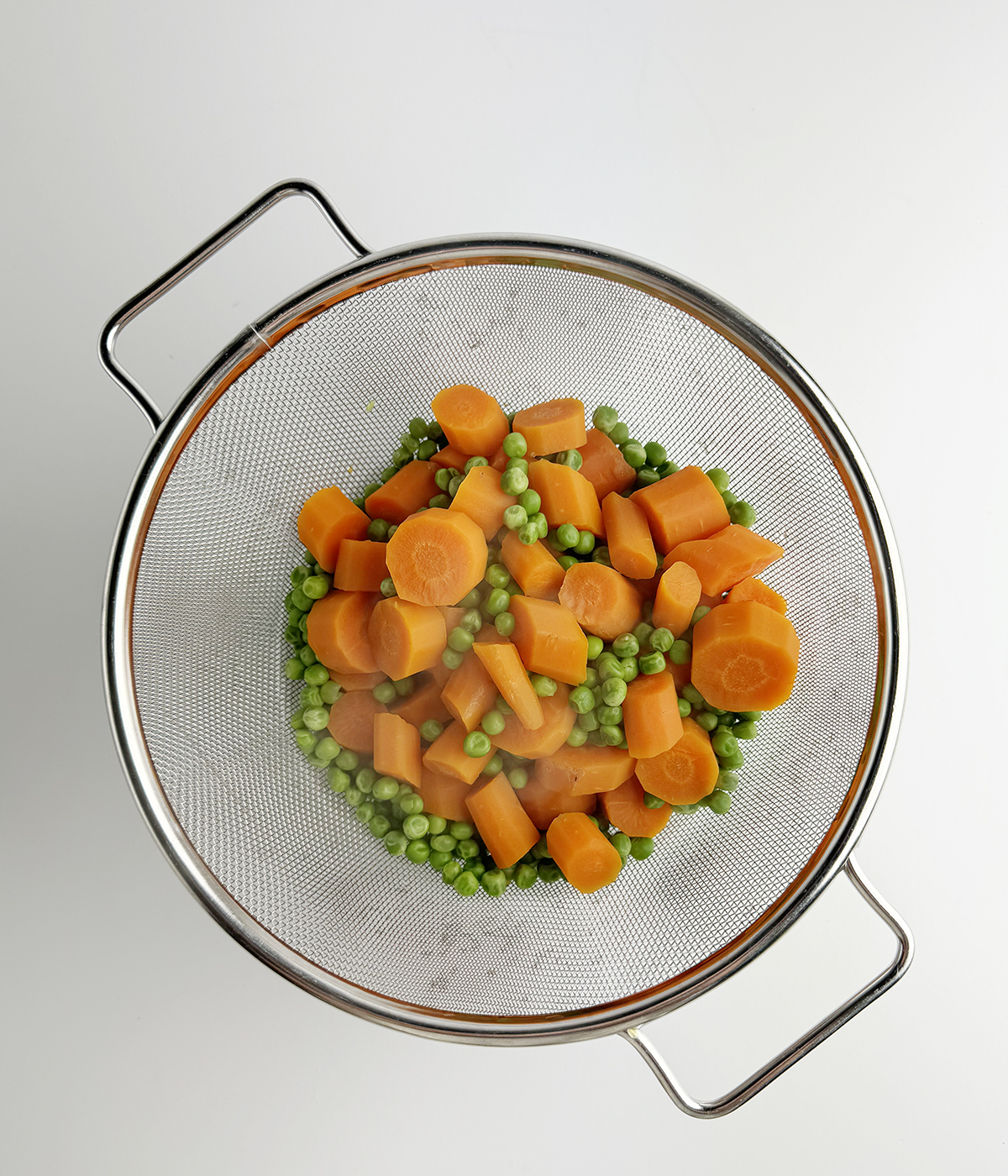 Peas and carrots draining in a strainer.