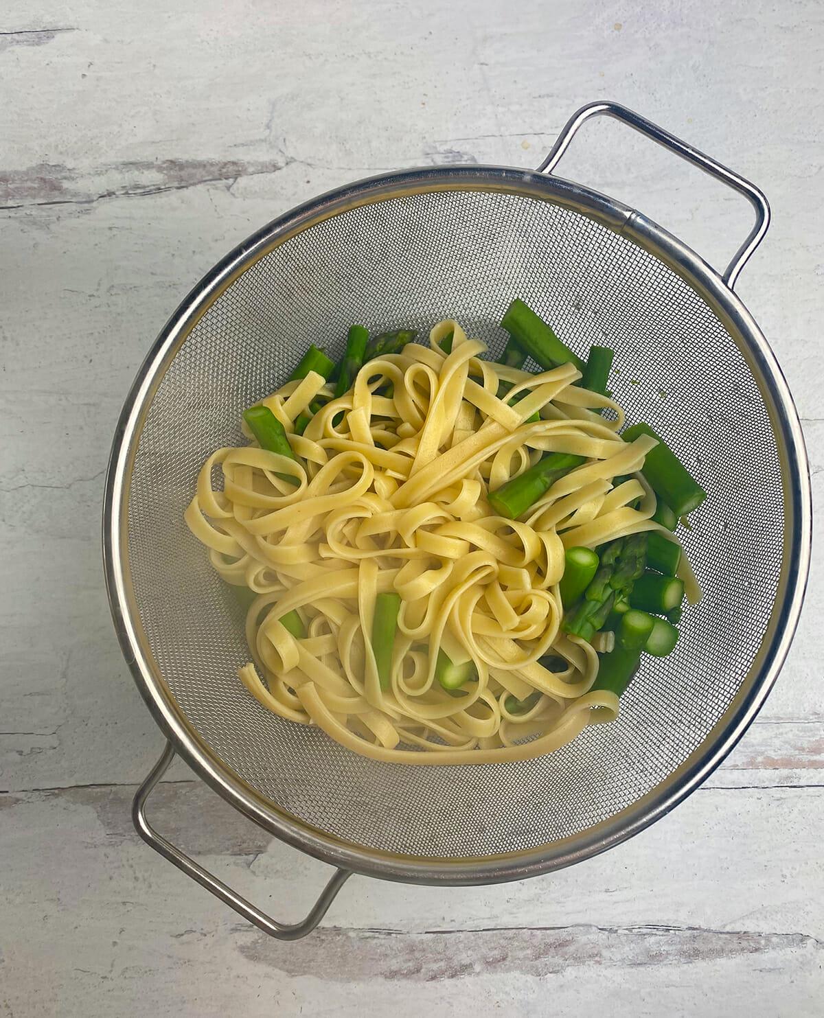 Drained pasta and asparagus in a strainer.