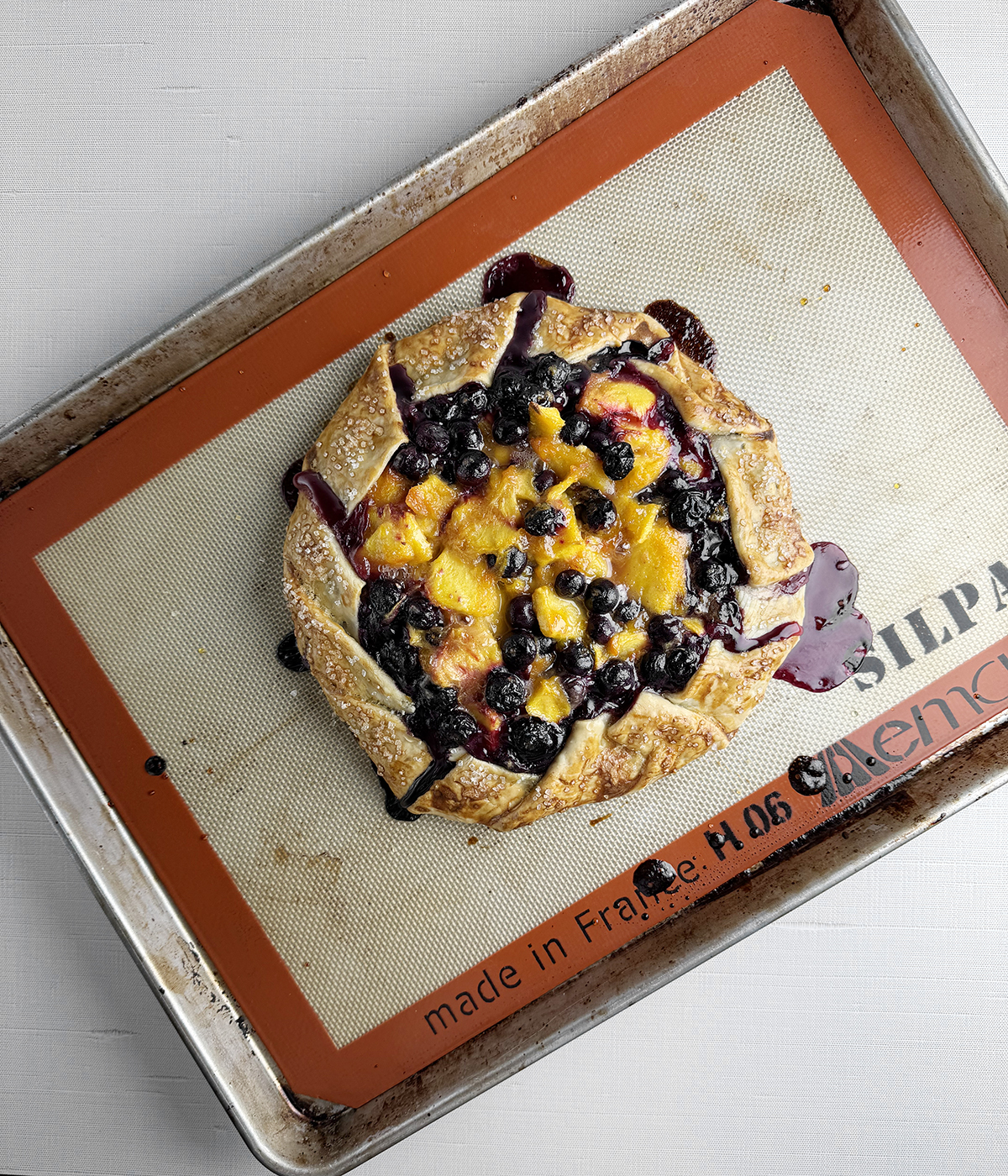 Baked blueberry peach tart on a baking pan.