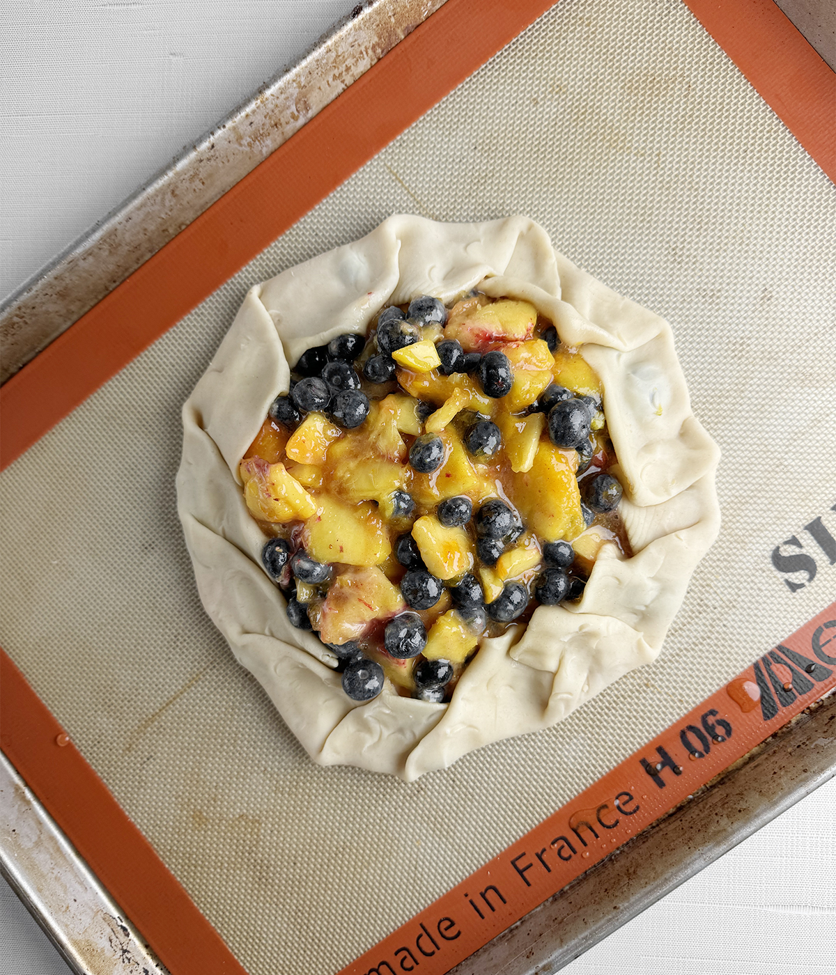 Blueberry peach tart with folded crust on a baking pan.