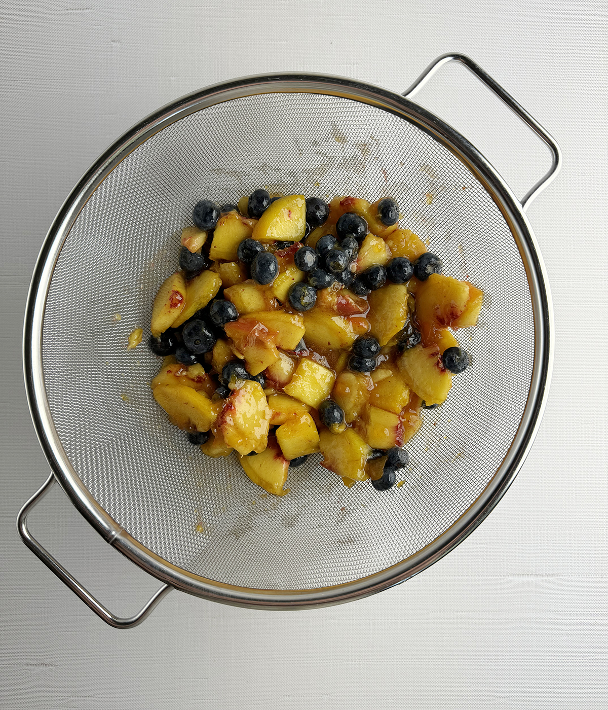 Peach and blueberry mixture draining in a strainer.