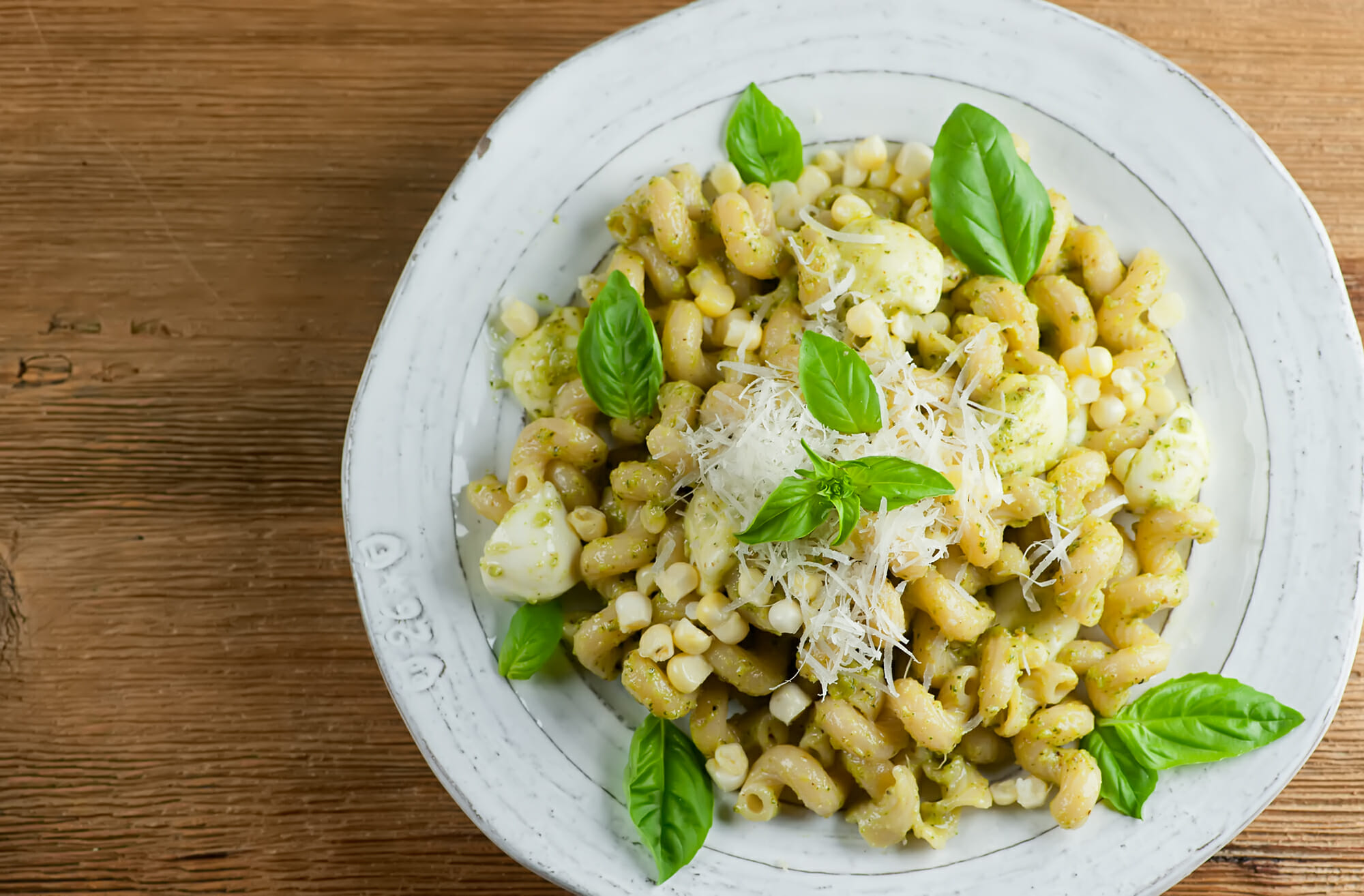 Plate of pesto pasta with fresh corn and mozzarella.