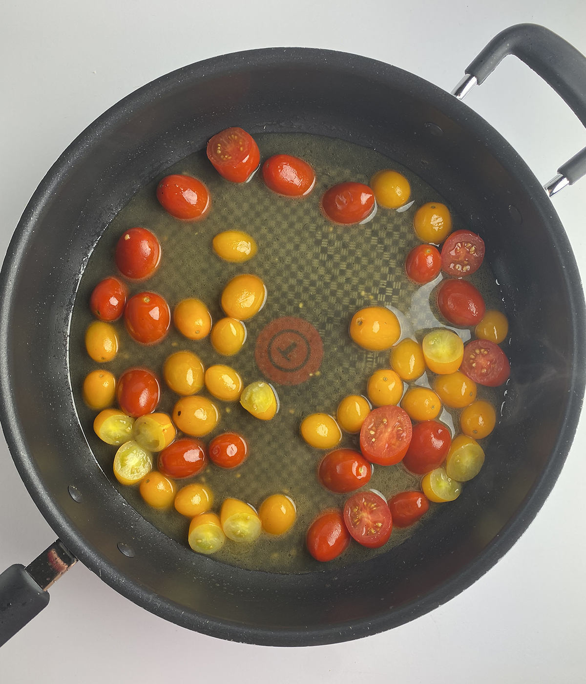 Cherry tomatoes cooking in a skillet.
