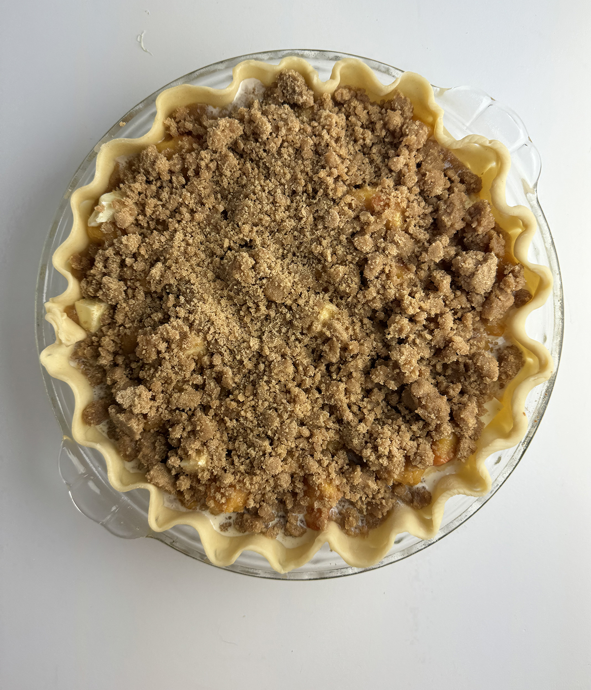 Fresh peach pie with crumble topping ready for the oven.