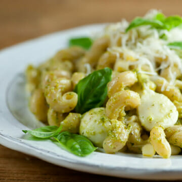 Pesto pasta with mozzarella and corn on a plate.