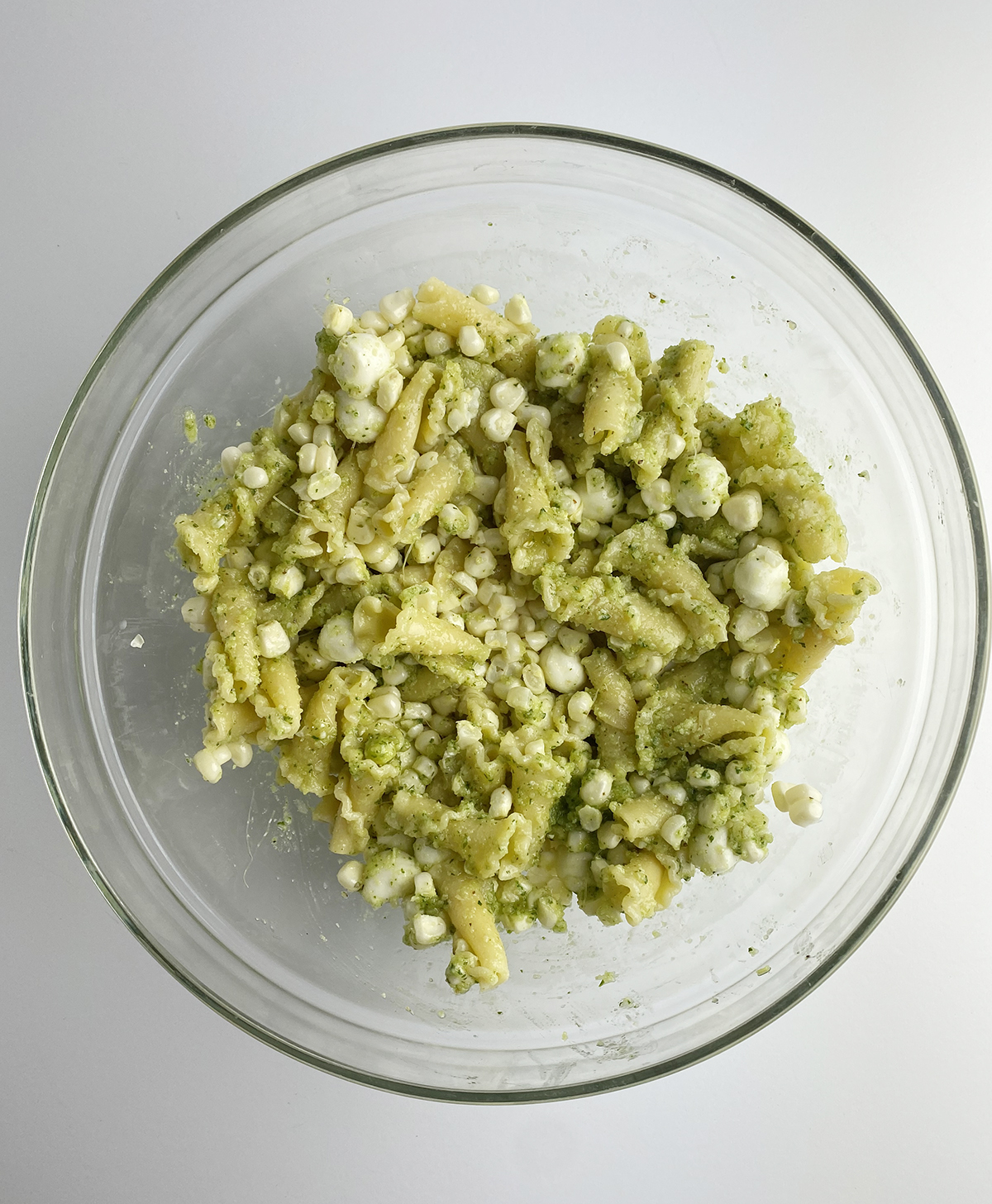 Pasta mixed with pesto and corn in a mixing bowl.