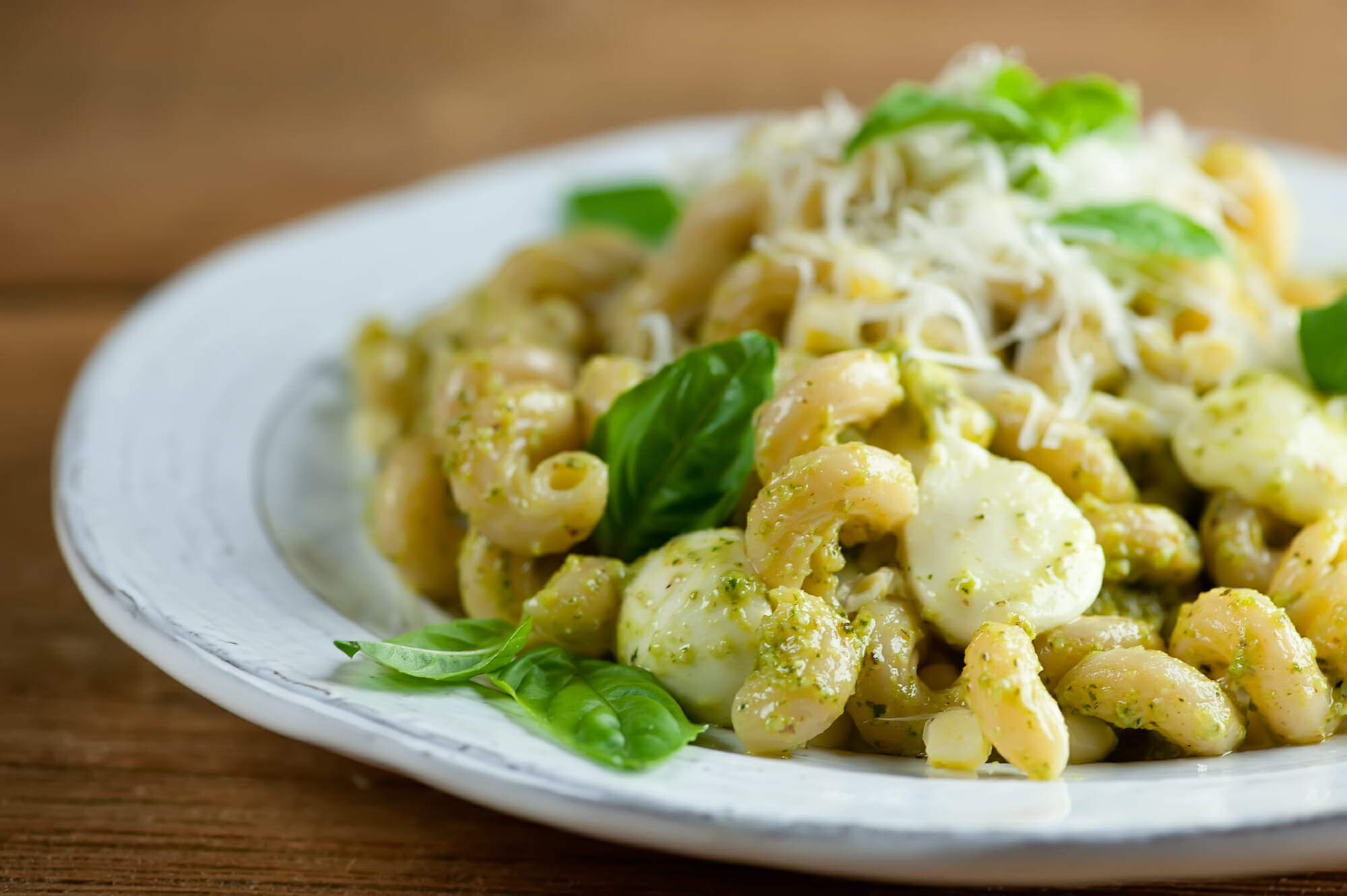 summer pasta recipe with pesto, corn and mozzarella Pesto pasta with fresh corn and mozzarella on a plate.