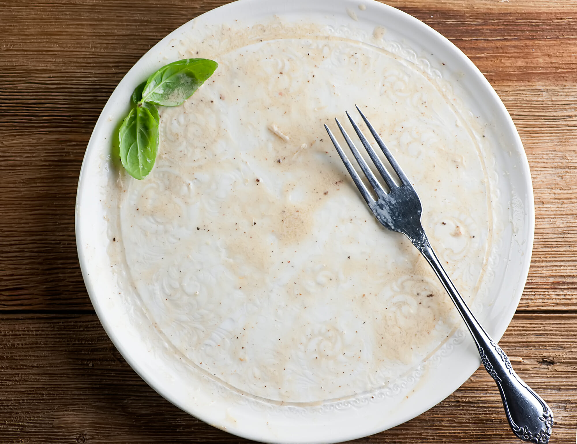 Empty pasta plate with a fork and a sprig of basil.