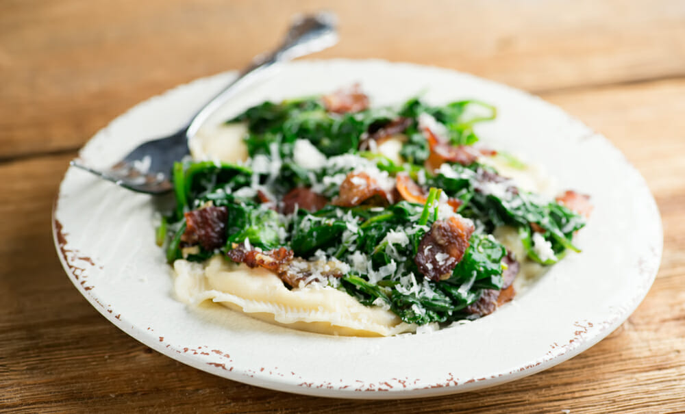 Plate of easy ravioli with baby spinach and bacon.