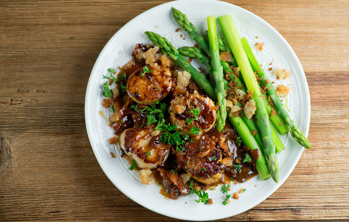 Scallops in maple cream sauce with asparagus on a plate.