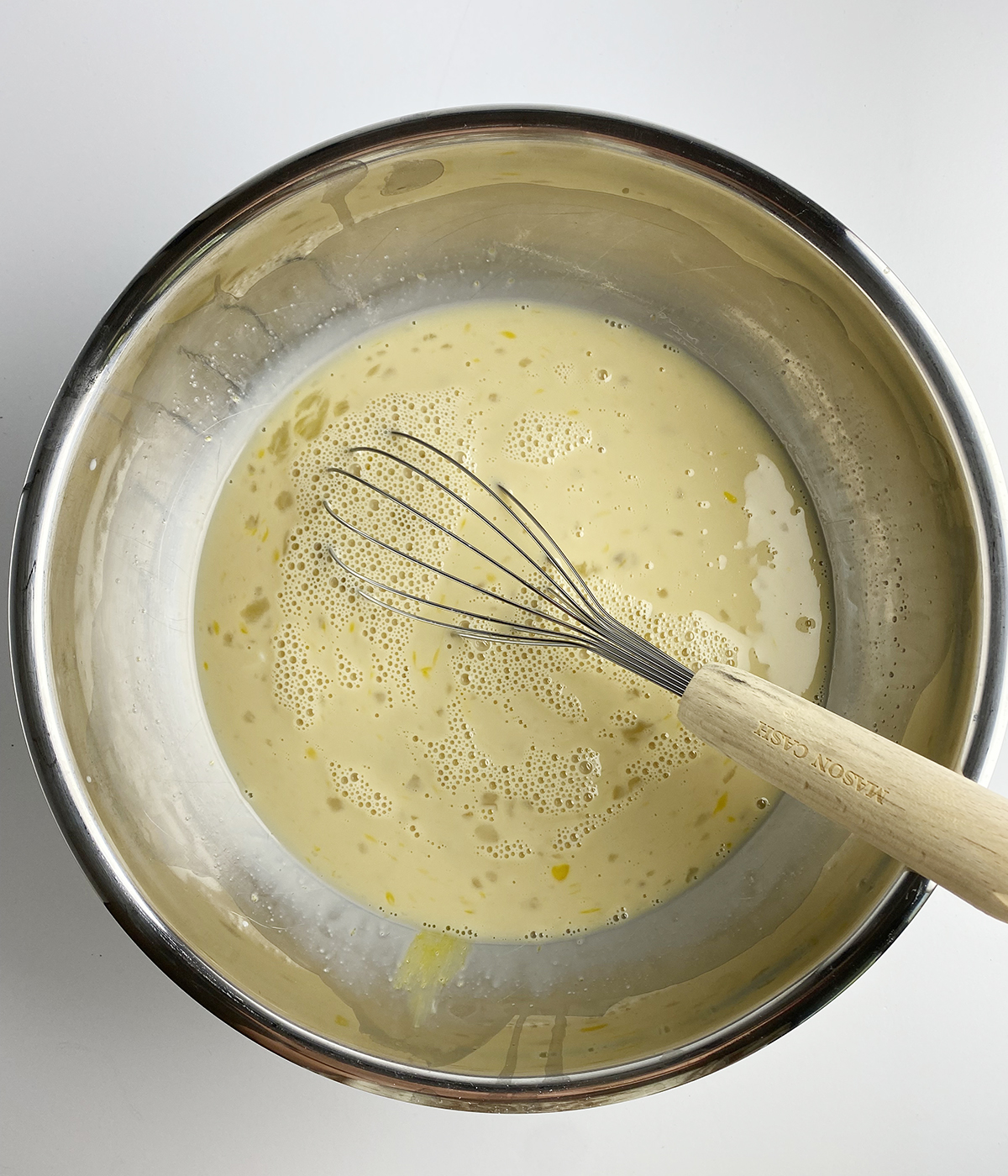 Egg and milk mixture in a bowl with a whisk.