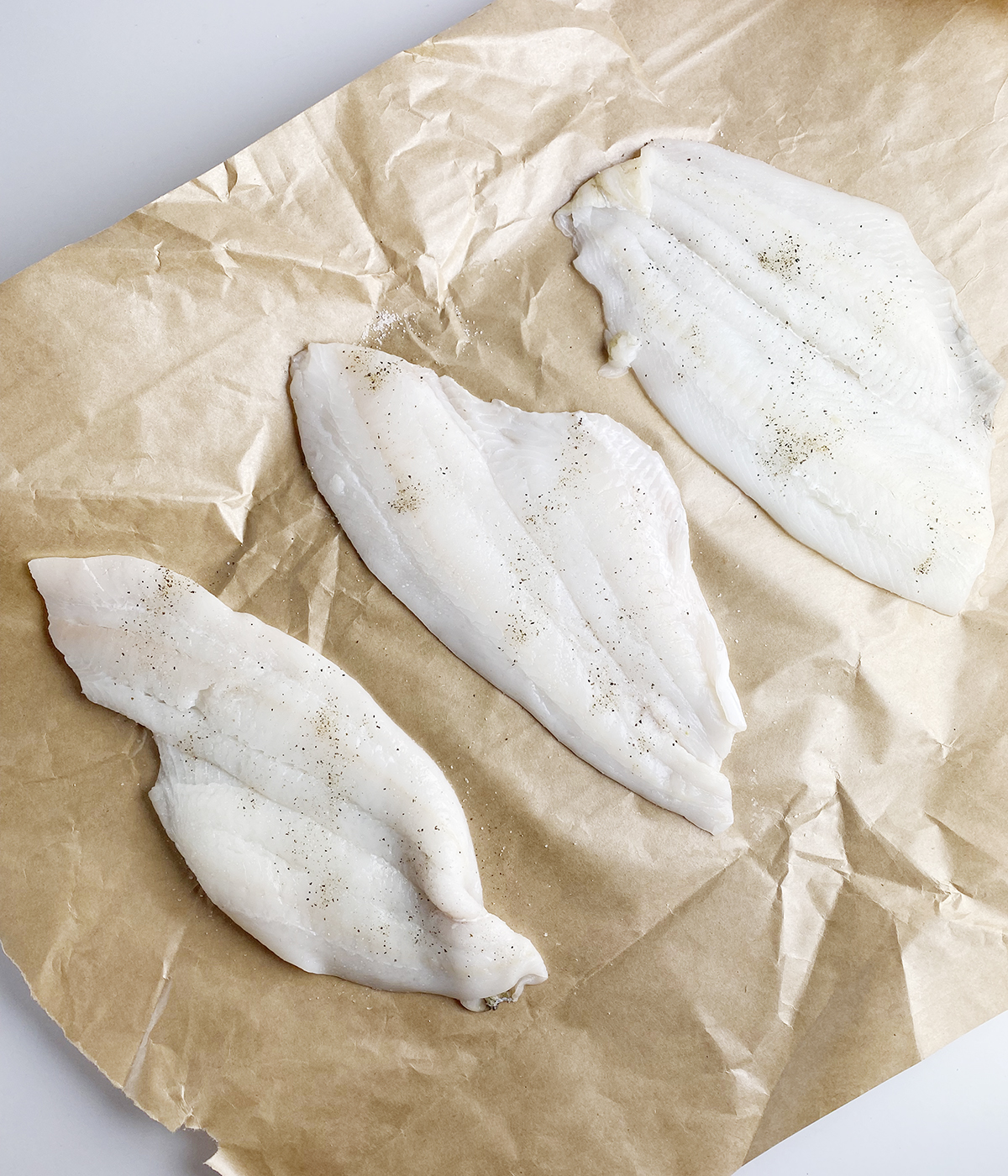 Filet of sole pieces seasoned with salt and pepper on a piece of parchment paper.