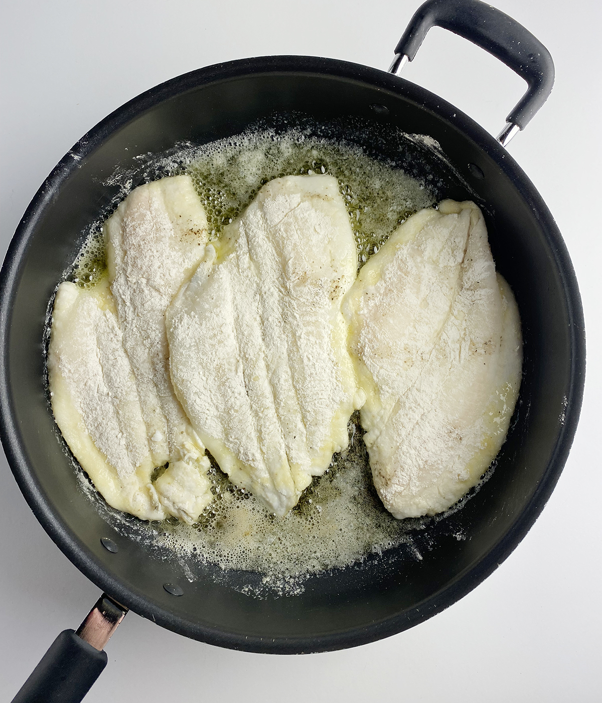 Flour covered filet of sole cooking in a skillet.