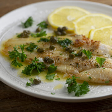 Julia Child's filet of sole on a plate with lemon and capers.
