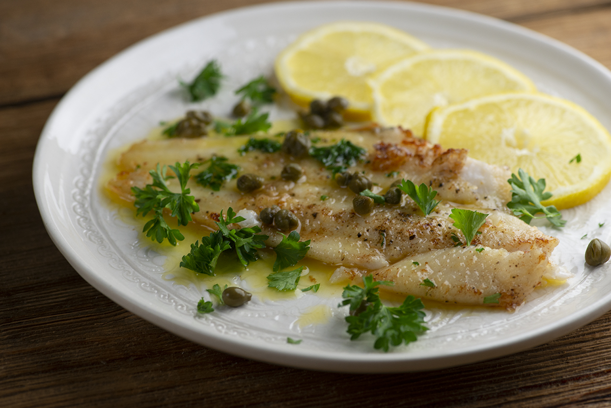 Julia Child's filet of sole on a plate with lemon and capers.